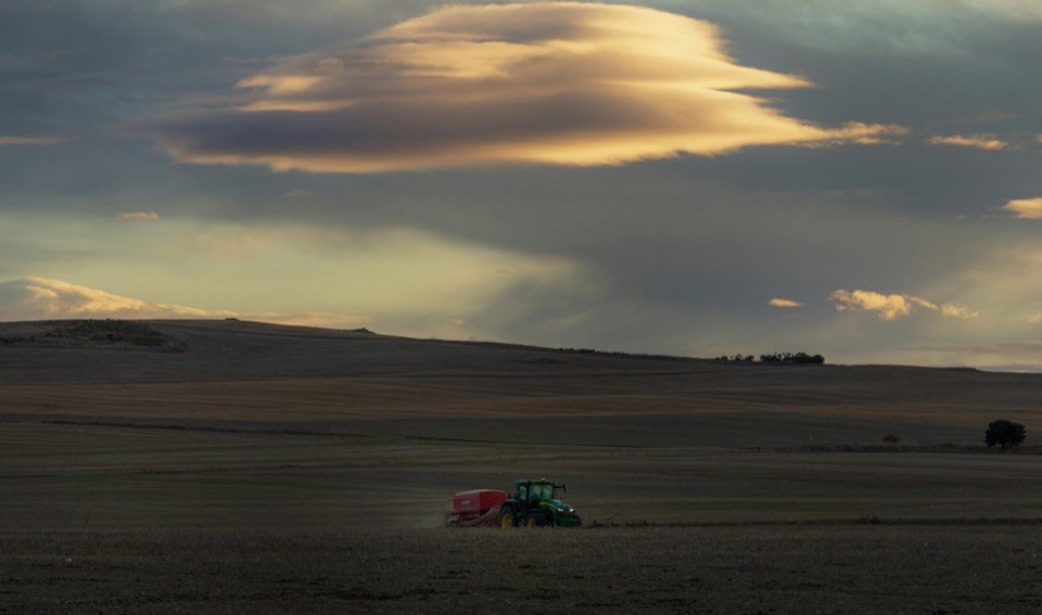 Tractor pulling a seed drill across an open field at dusk