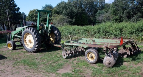 John Deere tractor fitted with a front loader and disc harrow for field tillage