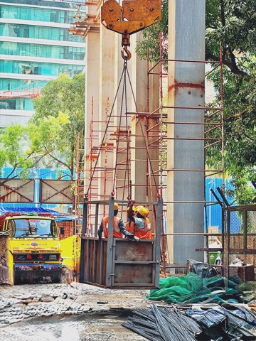 Crane lifting a steel cage with construction workers on a high-rise building site
