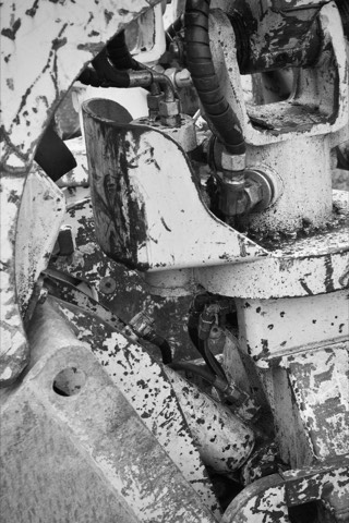 Black and white close-up of heavy machinery hydraulic rams, hoses and fittings